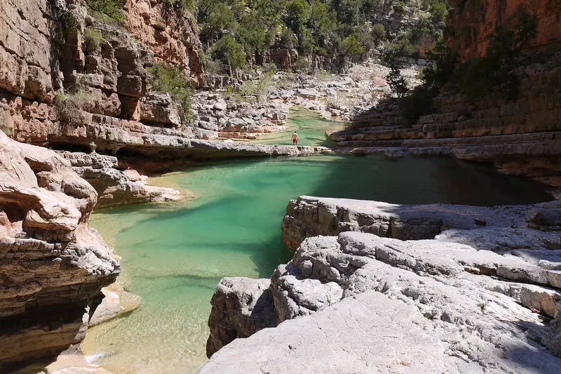 Turquoise pool between pale limestone ledges and red cliffs in Paradise Valley