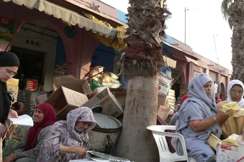 Women selling goods at stalls beneath awnings and palm trunks in Agadir's souk